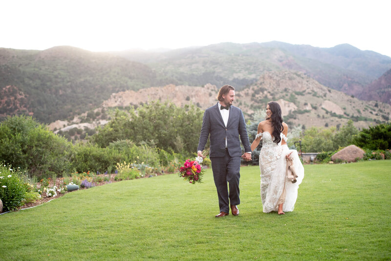 Newlyweds hold hands and smile at each other while walking in a garden lawn