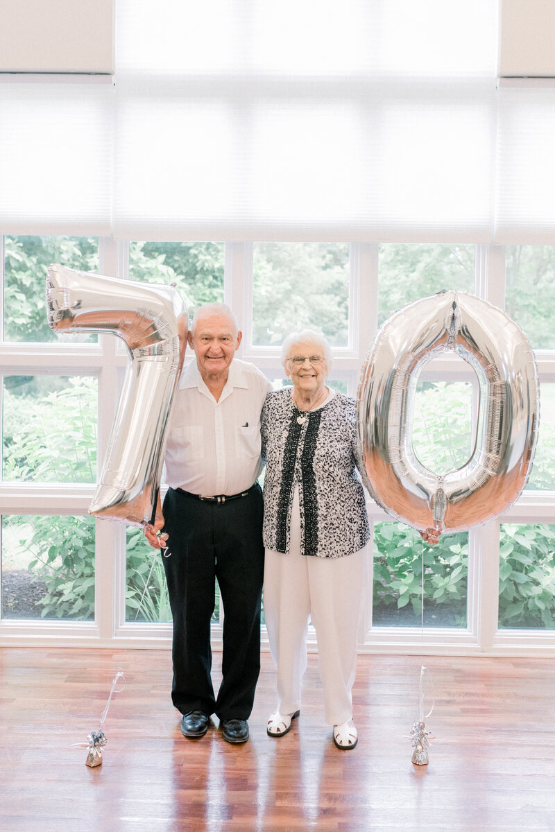 older couple holding 70 balloons to celebrate anniversary