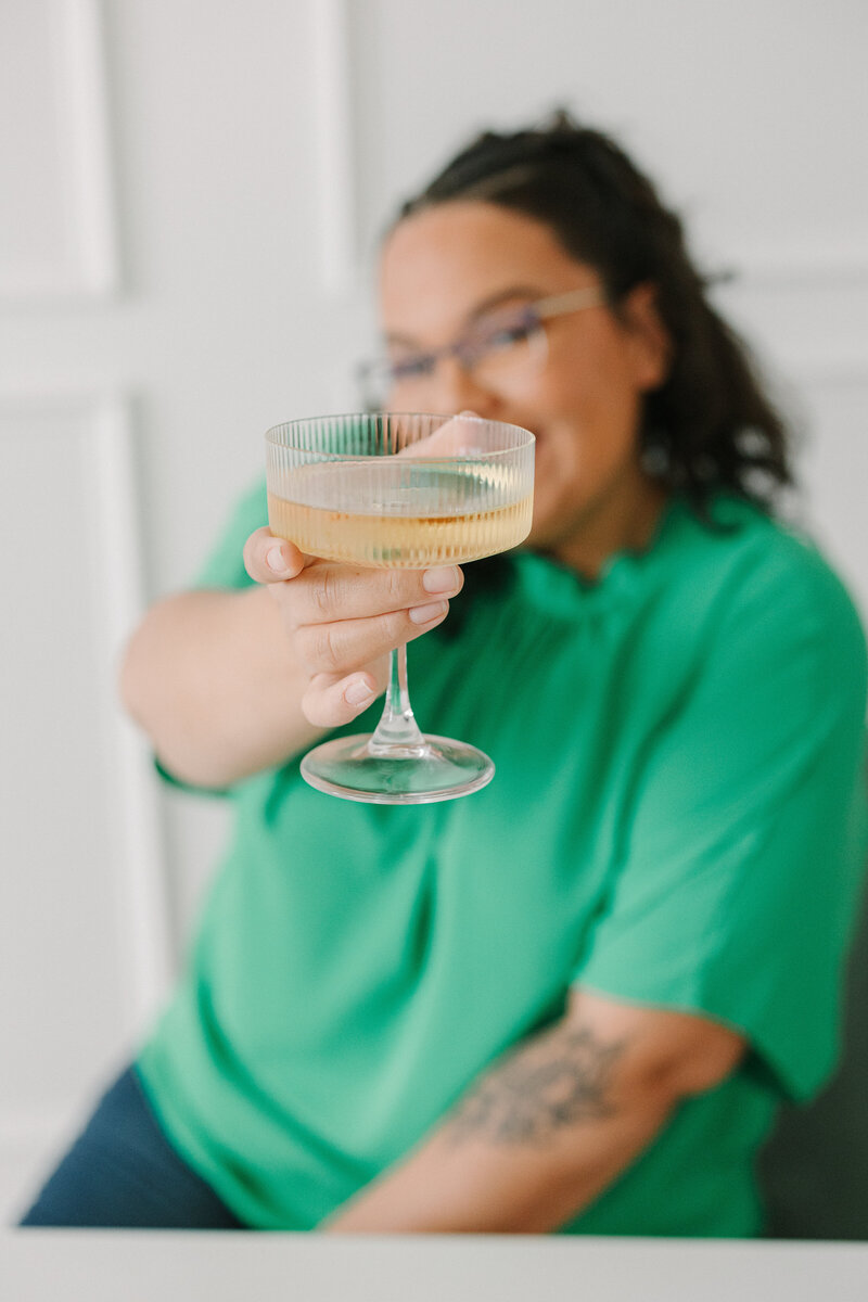 A person smiling and holding out a cocktail glass