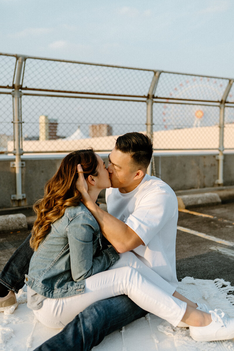 couple sitting on a skateboard facing each other staring into one anothers eyes, the girl holding the guys face with her hands