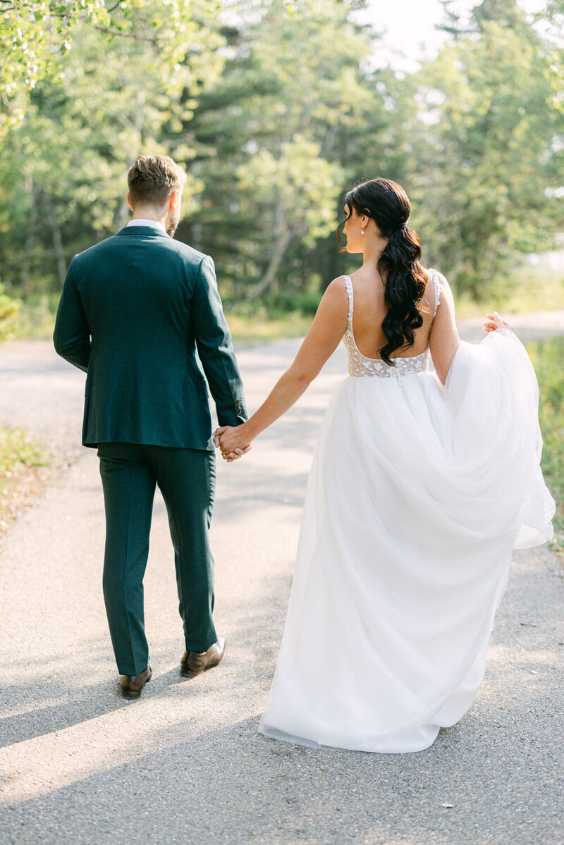 This romantic photograph captures the bride and groom walking hand in hand at Pinebrook Golf & Country Club, surrounded by beautiful scenery on their wedding day.