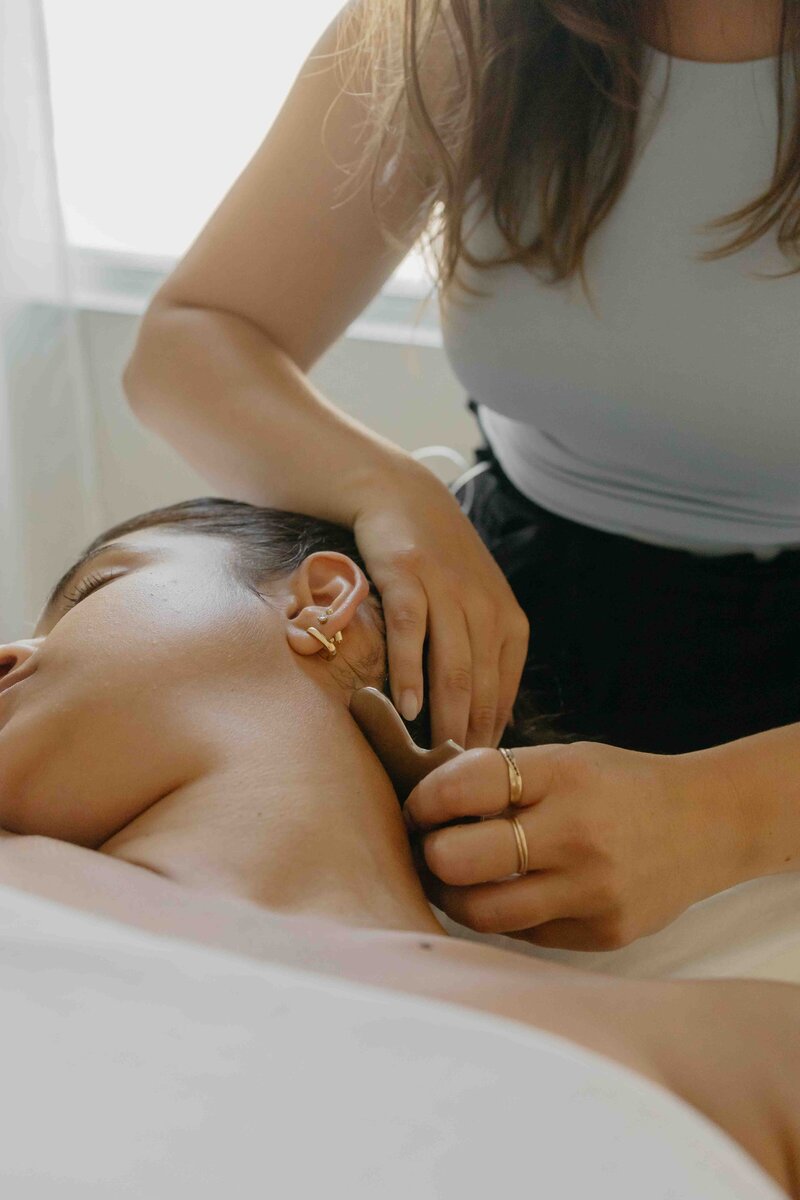 Femme allongée sur une table recevant un traitement de gua sha par une acupunctrice