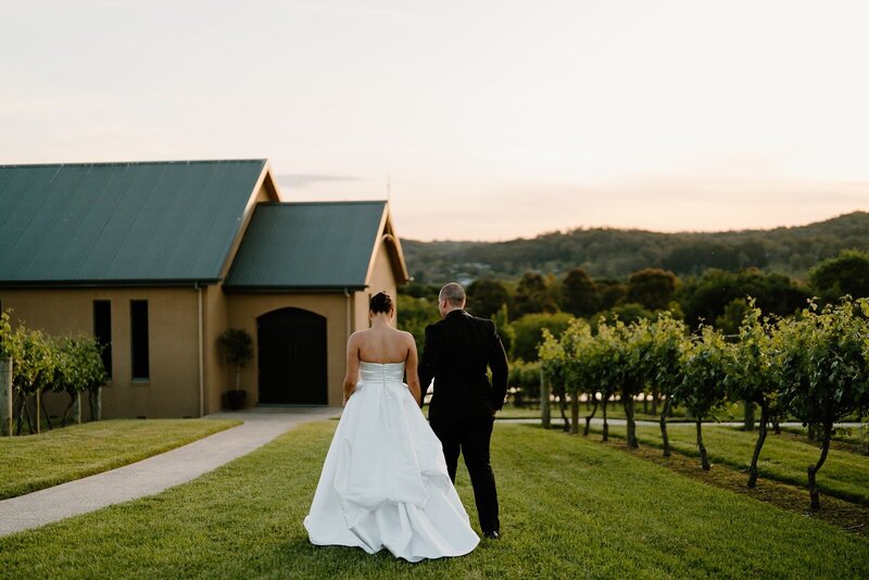 A couple on their wedding day walking along vineyards towards an old building