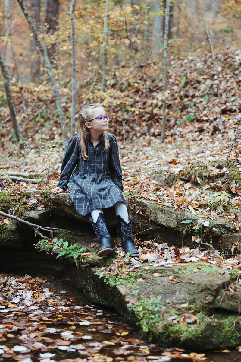 Little girl sitting on a rock looking around surrounded by leaves. 