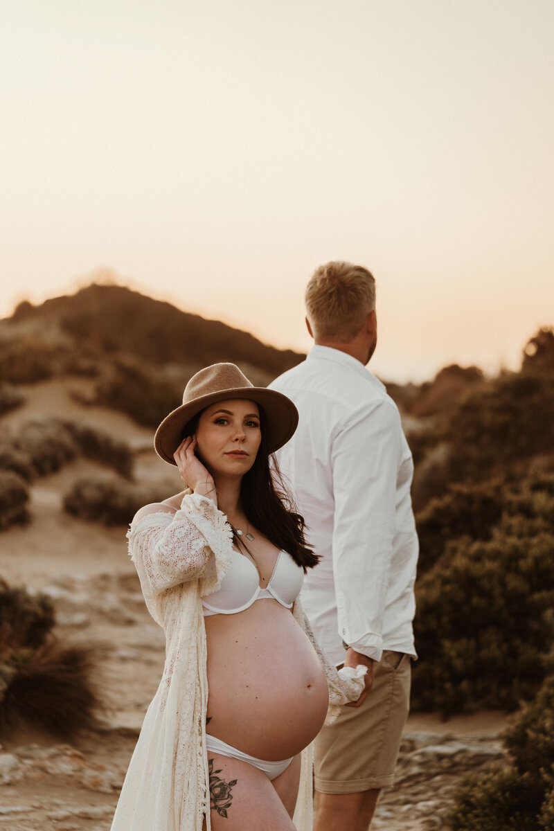 Maternity Photography, couple on the beach with pregnant woman looking toward the camera and man looking away