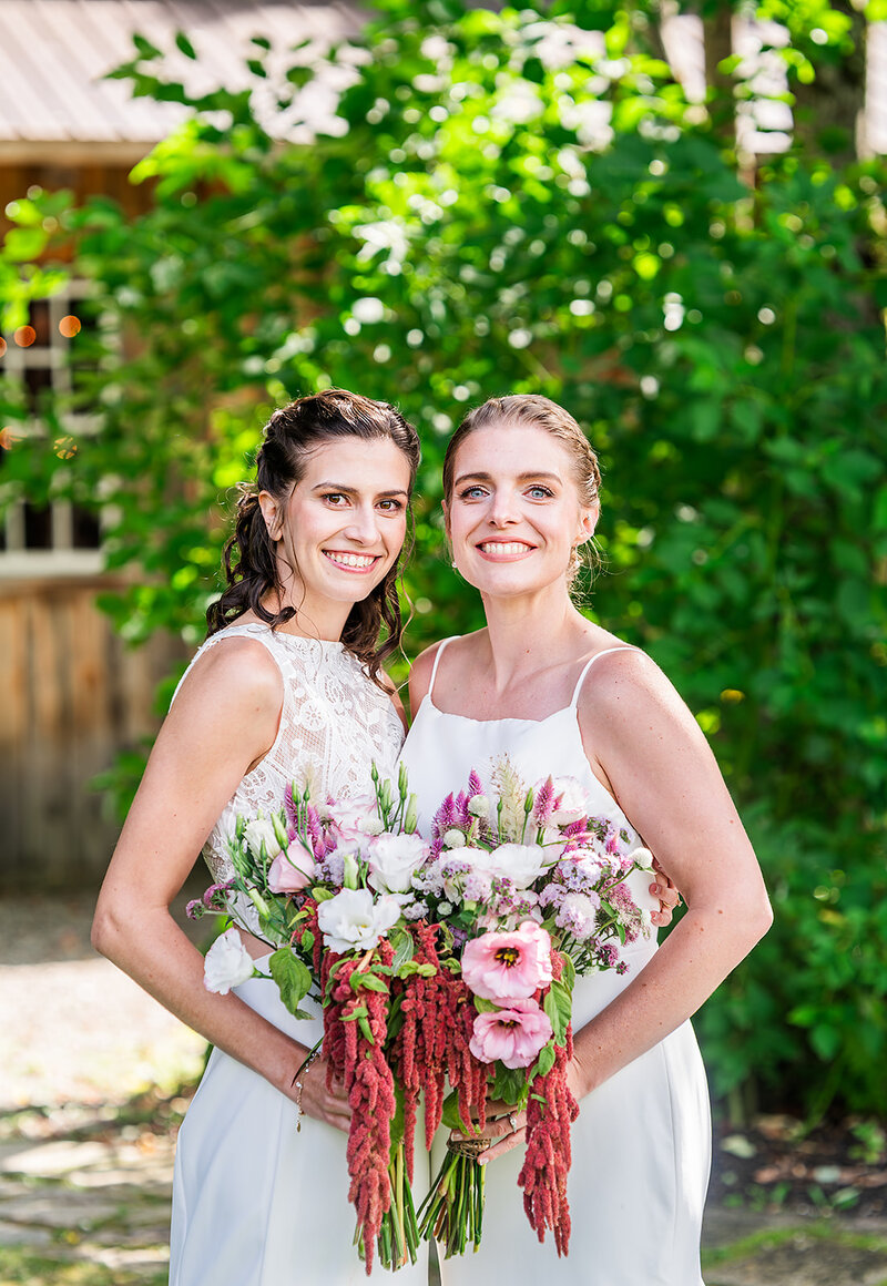 brides looking at camera on their wedding day with colorful floral bouquets