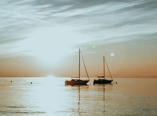 Segelyacht von oben auf dem Meer in tükisblauen Wasser und vier Menschen auf Luftmatratzen im Wasser