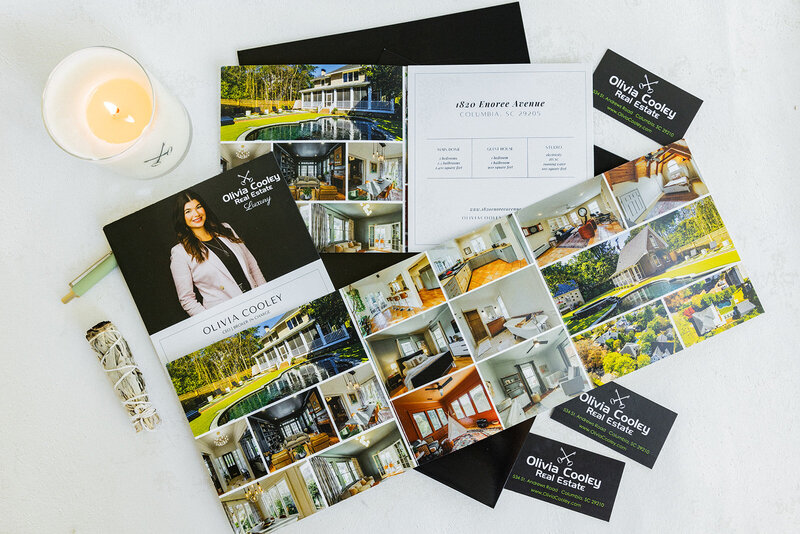 This branding photograph showcases high-end real estate marketing materials for Olivia Cooley Real Estate. The elegant presentation of brochures, business cards, and property details emphasizes professionalism and luxury in Columbia, SC's real estate market. This image is ideal for real estate professionals looking to elevate their brand through polished, cohesive visual storytelling.