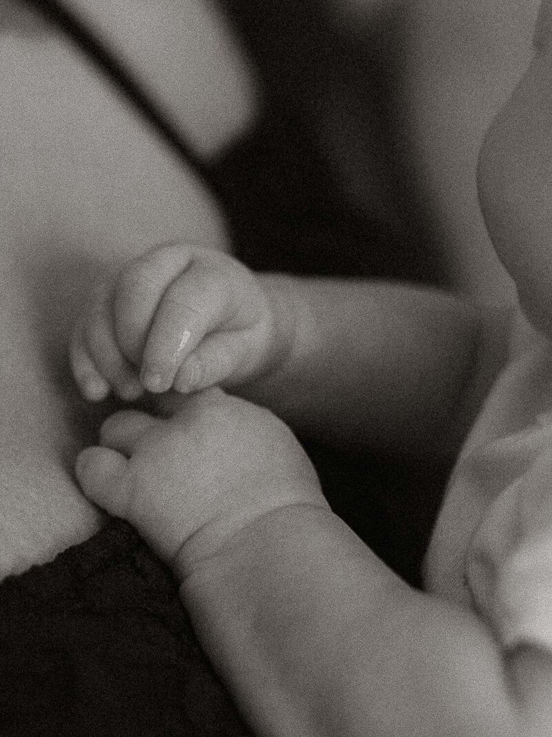 Black and white detail of a newborn’s tiny hands resting gently against their mother’s chest during an in-home Riverside session.