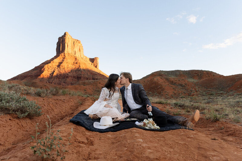 Moab elopement by wedding photographer Rachel with a couple kissing and sitting on a blanket.