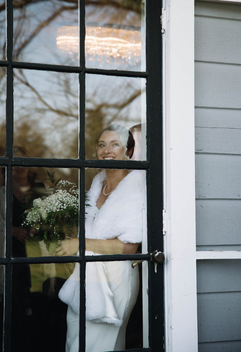 bride holding bouquet in wedding dress standing in window at whitehall mansion in brockport ny