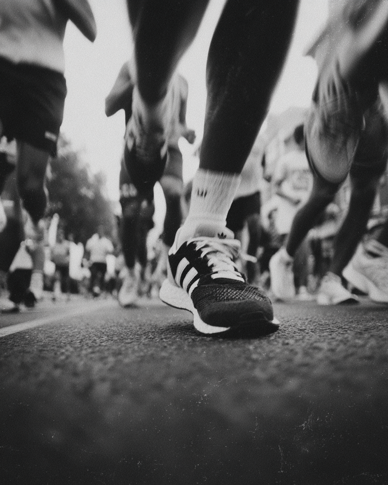 Vintage black and white photograph of people running in the street, close-up on their legs with sneakers, blurred background, grainy film filter, vintage aesthetic.2