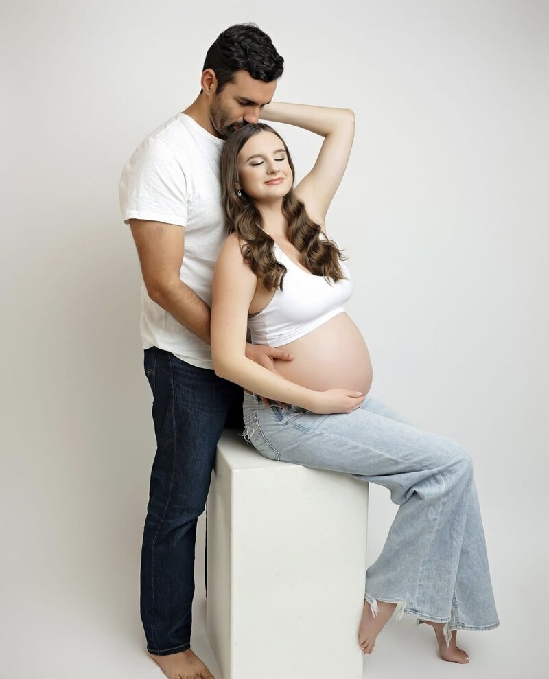 Maternity couple posed wearing white t-shirts and jeans.