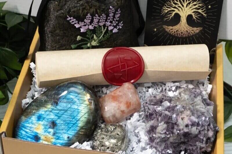  A spiritual gift box containing a scroll, crystals, a velvet pouch with lavender embroidery, and a card featuring a golden tree symbol.