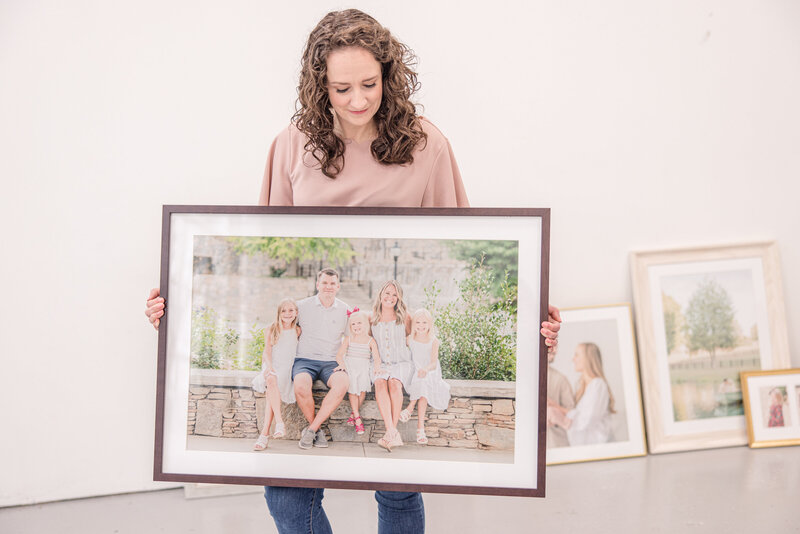 Jessie Modlin holding framed wall art and looking down at the piece with other fames in background