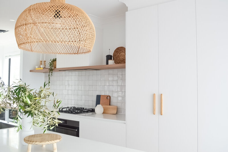 Minimalist kitchen with white cabinets, a wooden pendant light, and greenery on the counter, thoughtfully crafted by a Newcastle interior designer.