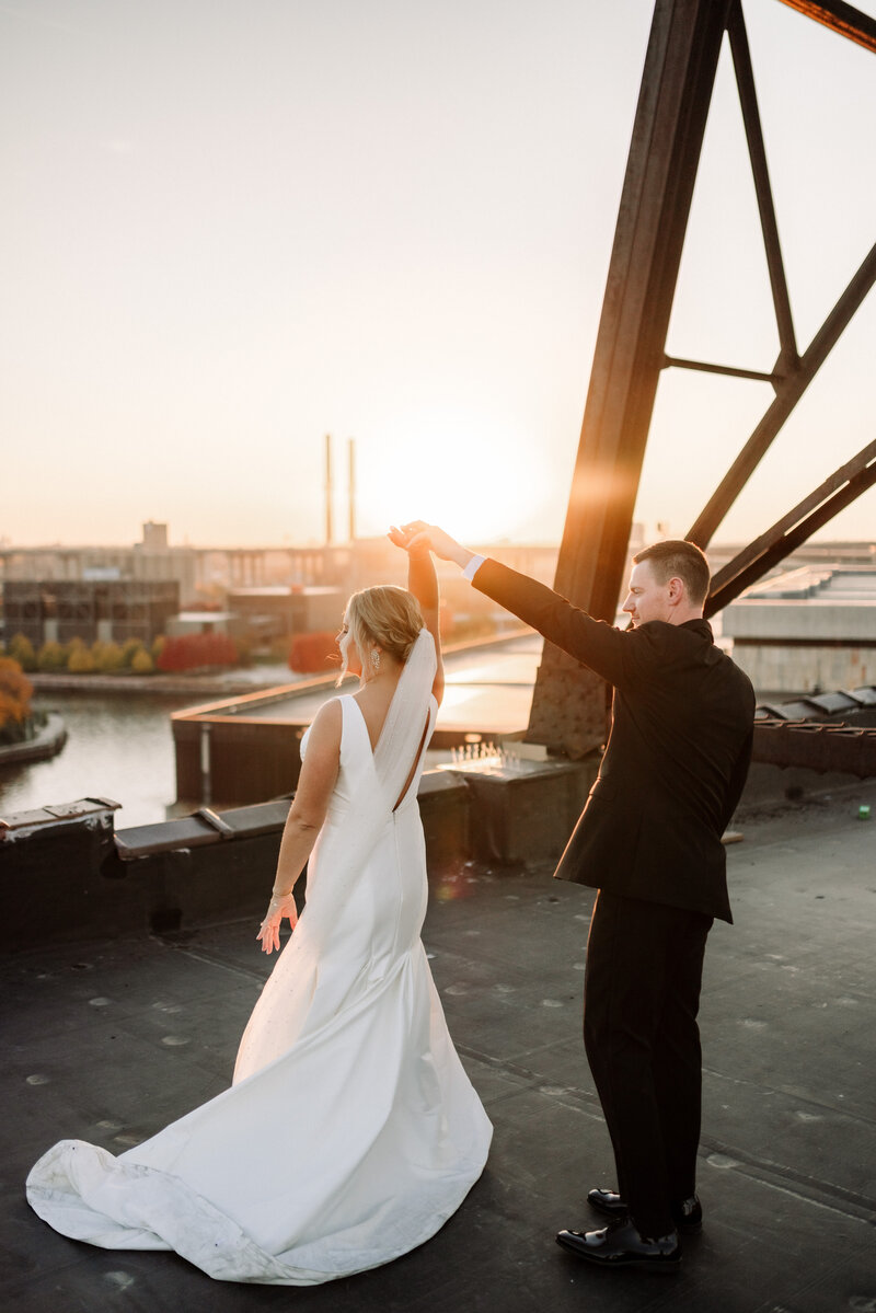 Bride and groom dance on top of a rooftop at sunset with a city view