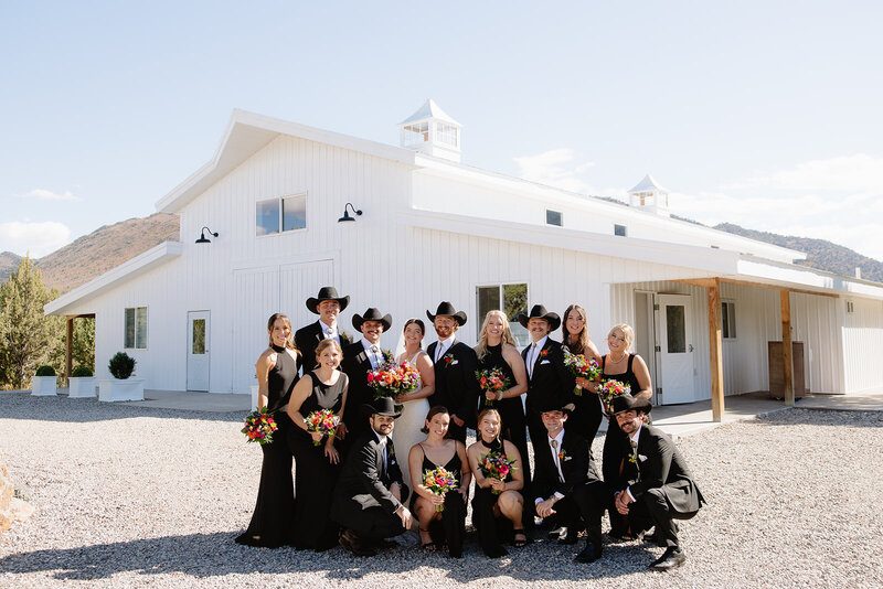A fun take on traditional wedding party photos. Black bridesmaids dresses and colorful florals and groomsmen with cowboy hats. 