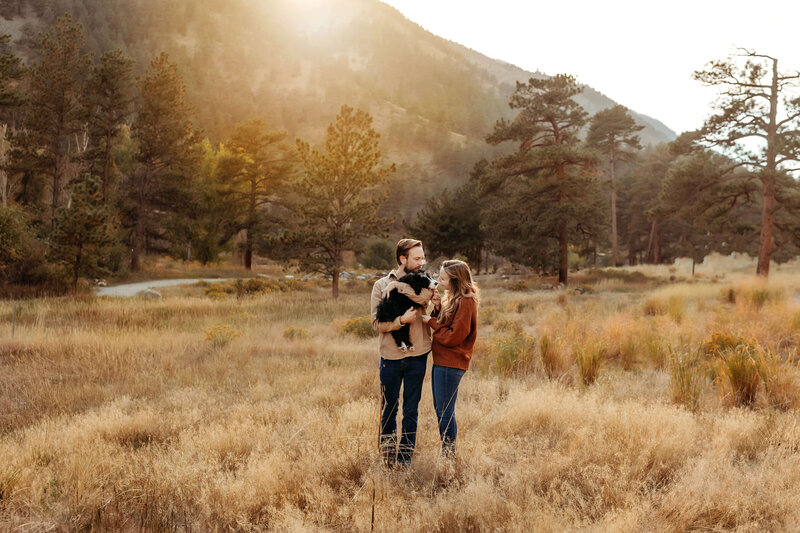 Husband, wife and puppy in a field at sunset in Loveland