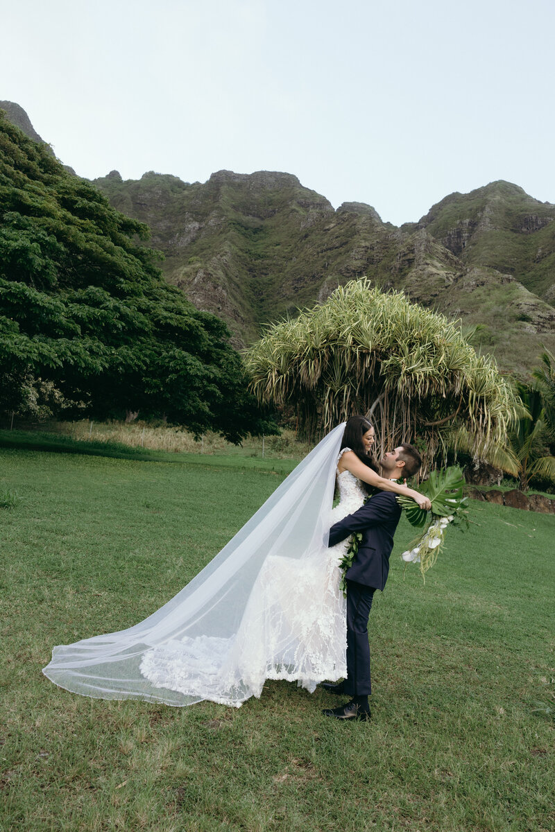 Bride and groom walking hand in hand at Kualoa Ranch with mountain views in the background
