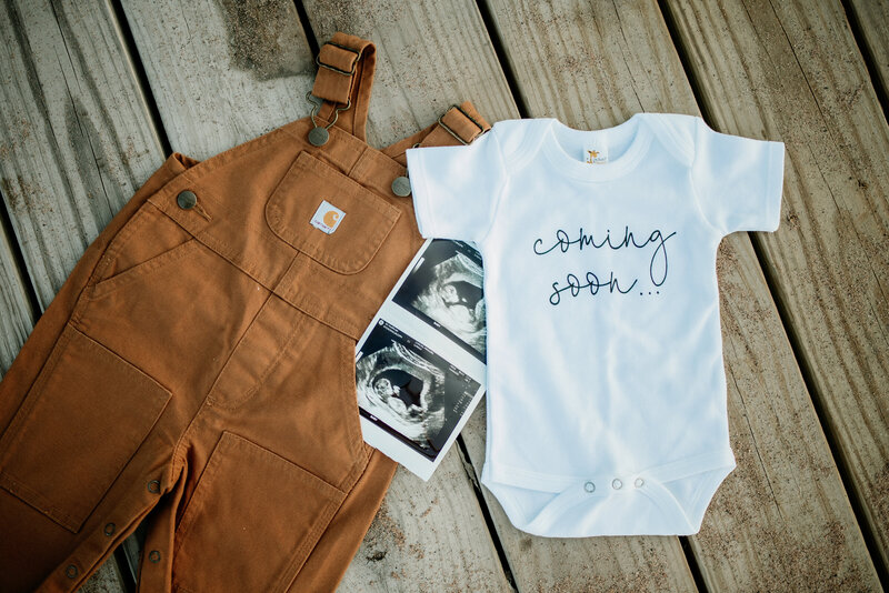 Country pregnancy announcement idea featuring Carhartt overalls, an ultrasound, and a onesie with "coming soon" scrolled across it.