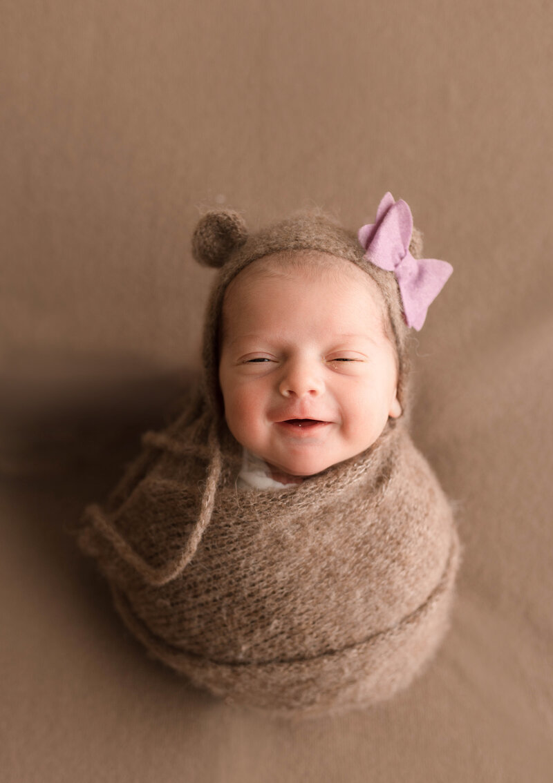 Baby wrapped in brown knit with bear bonnet smiling