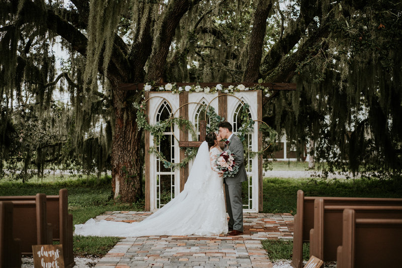 Wedding couple kiss under Spanish moss at their ceremony at Ever After Farms Ranch Wedding in Indiantown  FL