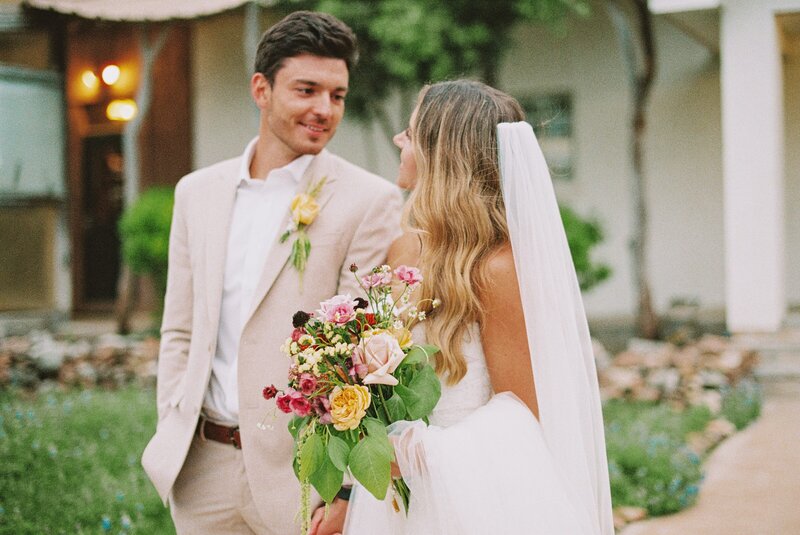 bride and groom smiling at each other holding her colorful bouquet