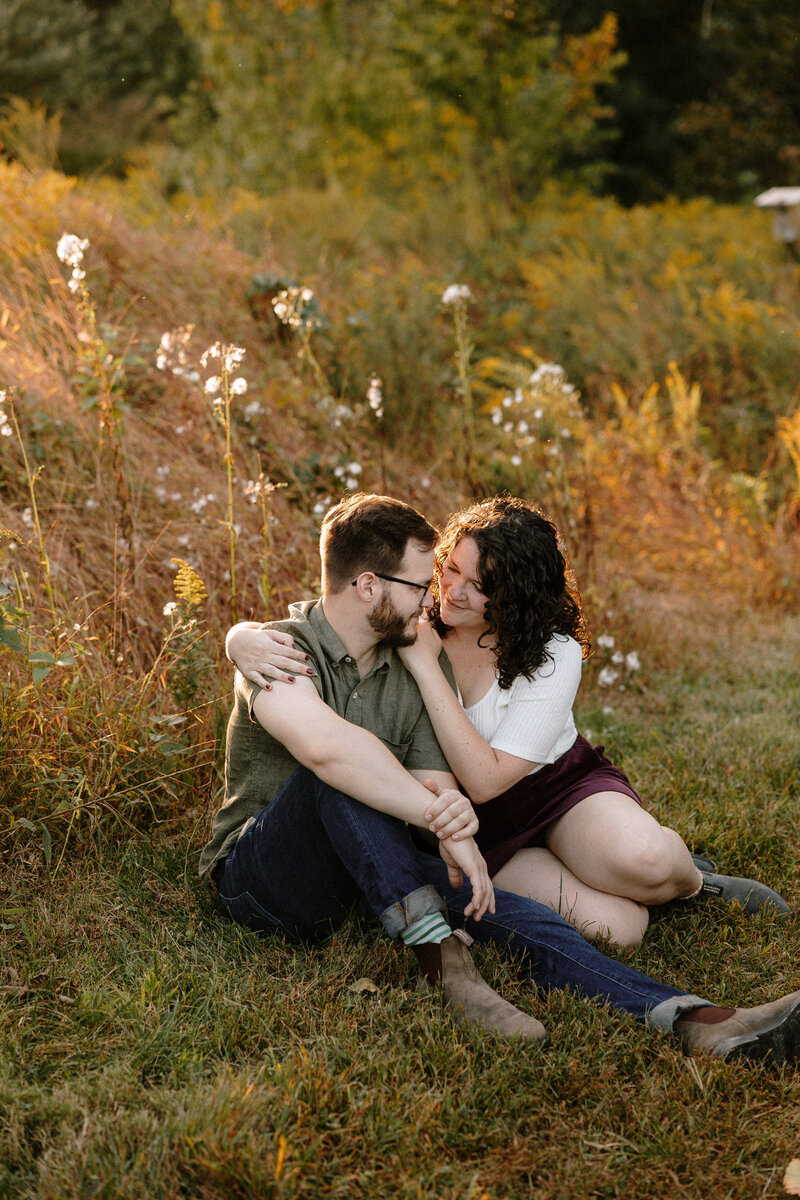 An engaged couple smiles at each other in a lush field, capturing a moment of love and happiness in nature.