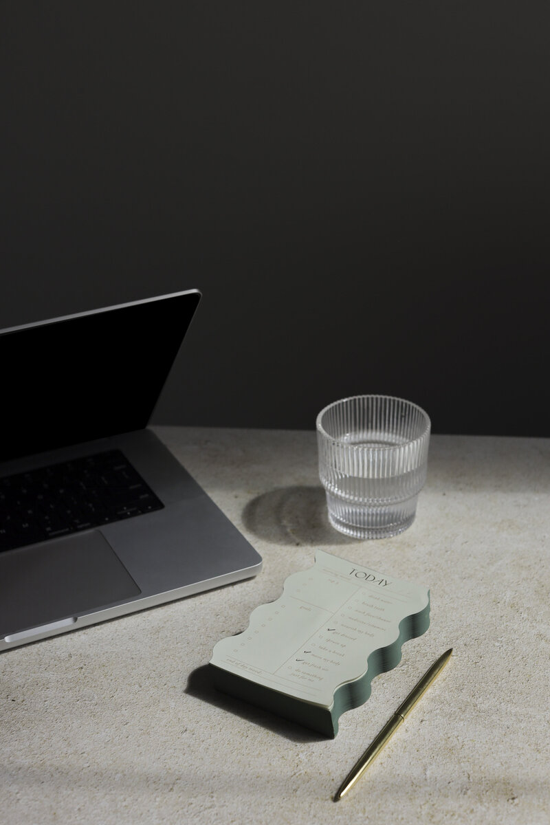 laptop on a desk with a glass of water, pen, and notepad
