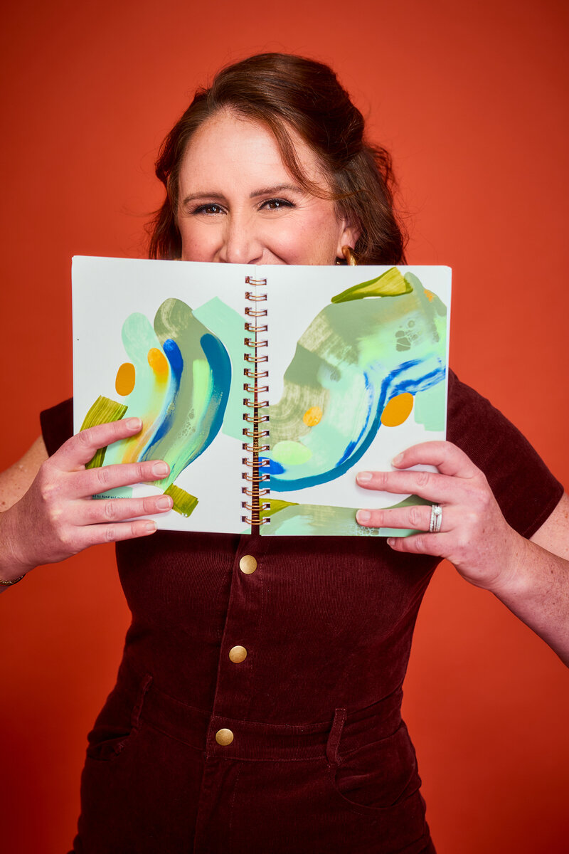 Jaime Bartol smiling behind a colorful abstract notebook, leadership coach blending creativity and strategy