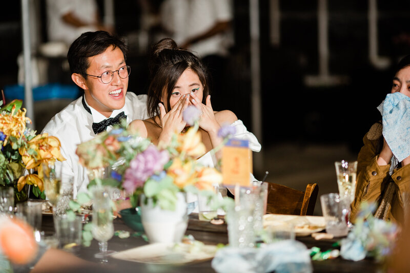 An emotional bride wipes away tears of joy and the groom laughs during the speeches at their wedding at Dos Pueblos Orchid Farm.