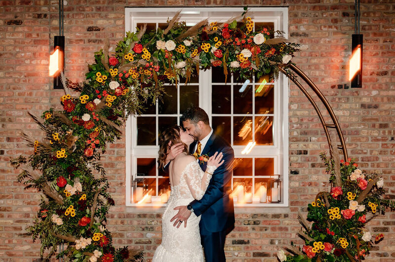 Bride and groom kiss at night in front of fall flowers at Loft Lucia
