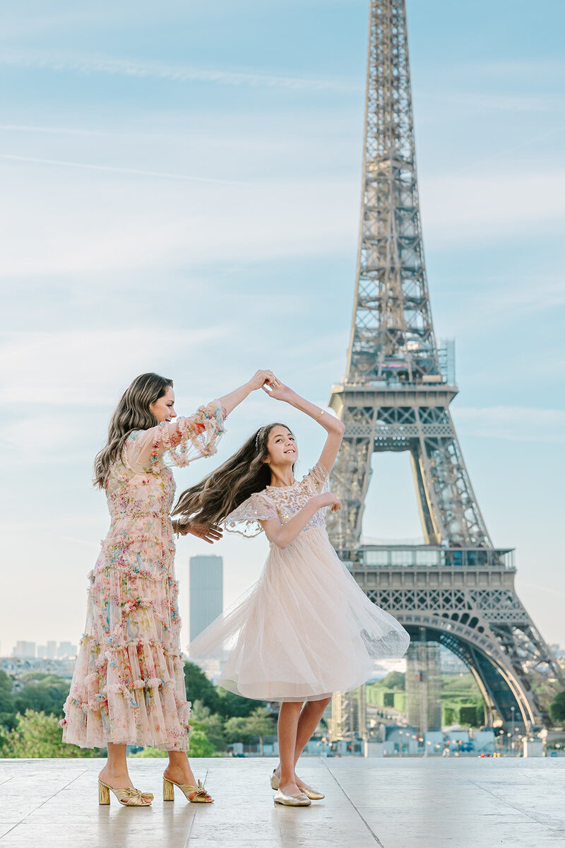 Mother and daughter dancing together in dresses near the Eiffel Tower at Trocadéro during a joyful Paris family photoshoot.