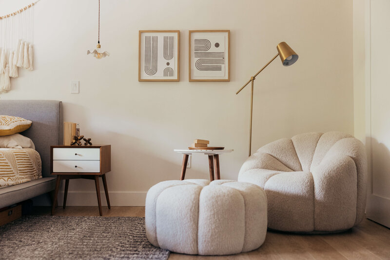 A seating area and artwork on the wall with part of the bed visible in a bedroom with boho-chic aesthetic, representing the eclectic home decor vibes by Winsome Home Interiors. 