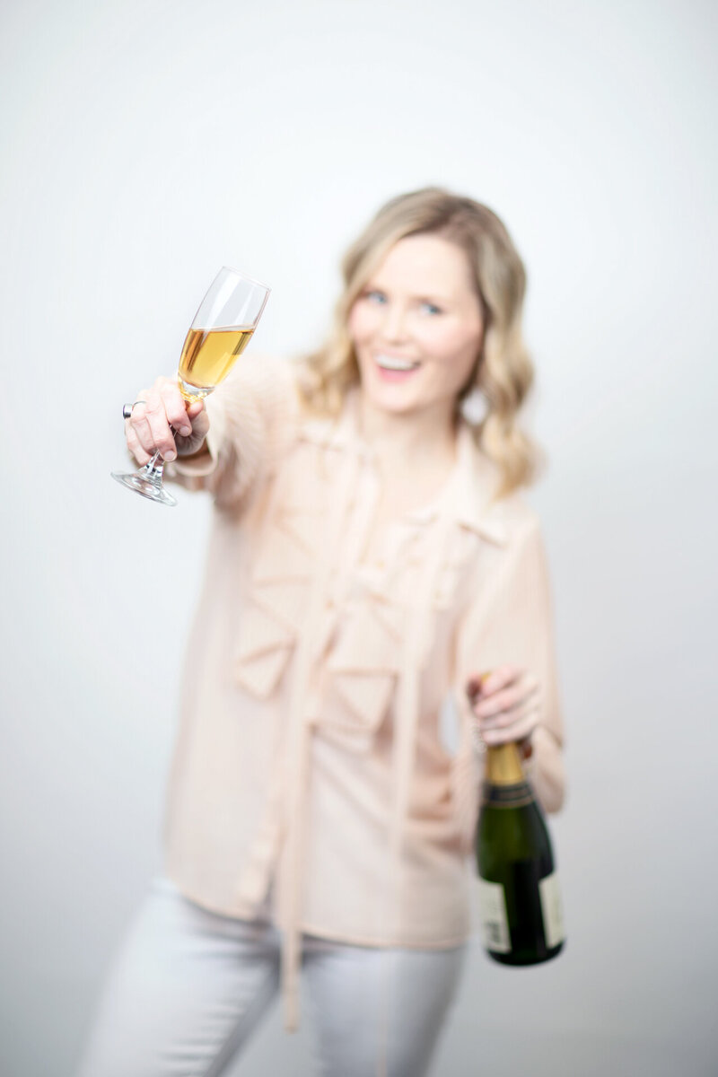 Photographer Alison McWhirter holding champagne bottle and holding up a glass to toast