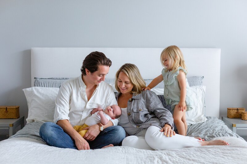family of four in fresh apparel sit on bed for newborn photos
