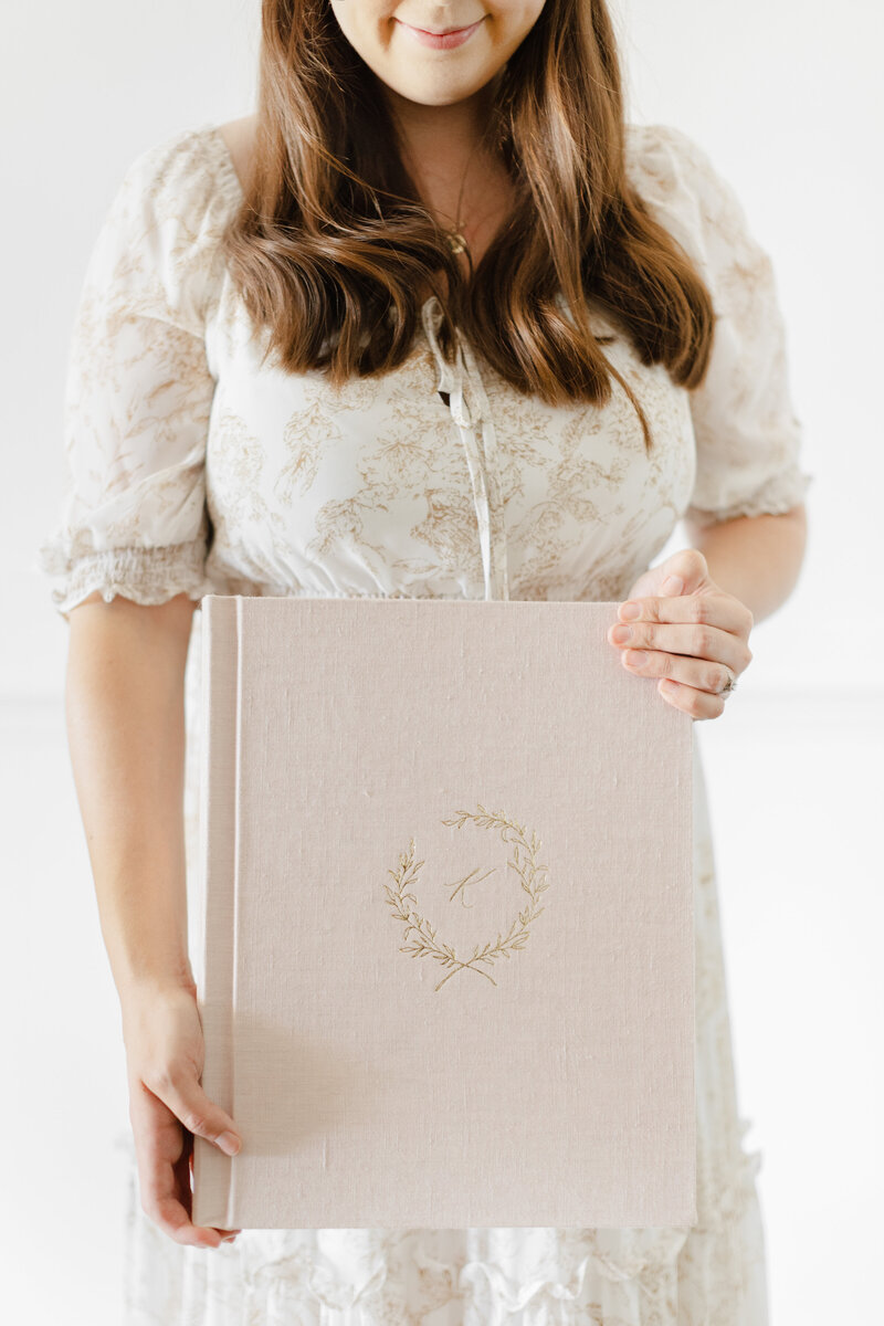 A photo of Newborn Photographer Washington DC holding a large pink heirloom album with gold debossing