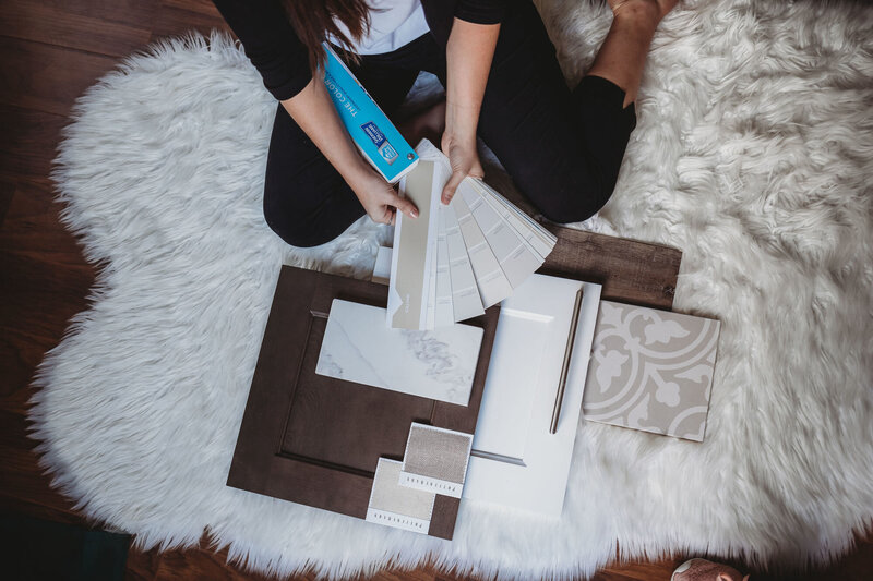 Woman comparing paint swatches from a Sherwin Williams paint fan to other selections for kitchen products like cabinets, countertops, tile and hardware.