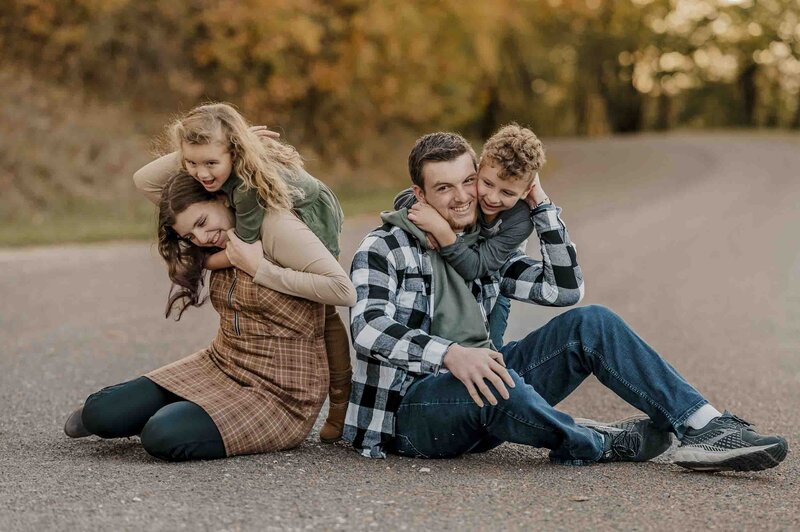 Four siblings wrestle with smiles on their faces with fall leaves in the background.