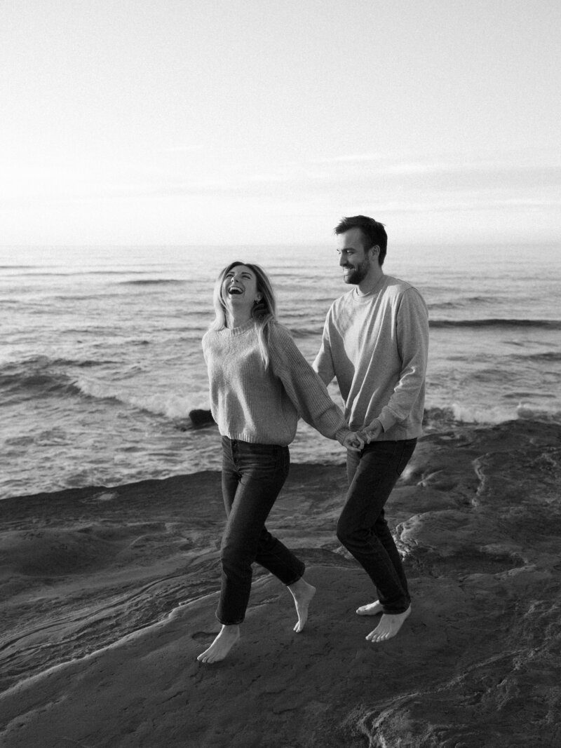 Couple running hand in hand at Sunset Cliffs in La Jolla, California, with dramatic coastal views and a golden sunset in the background.