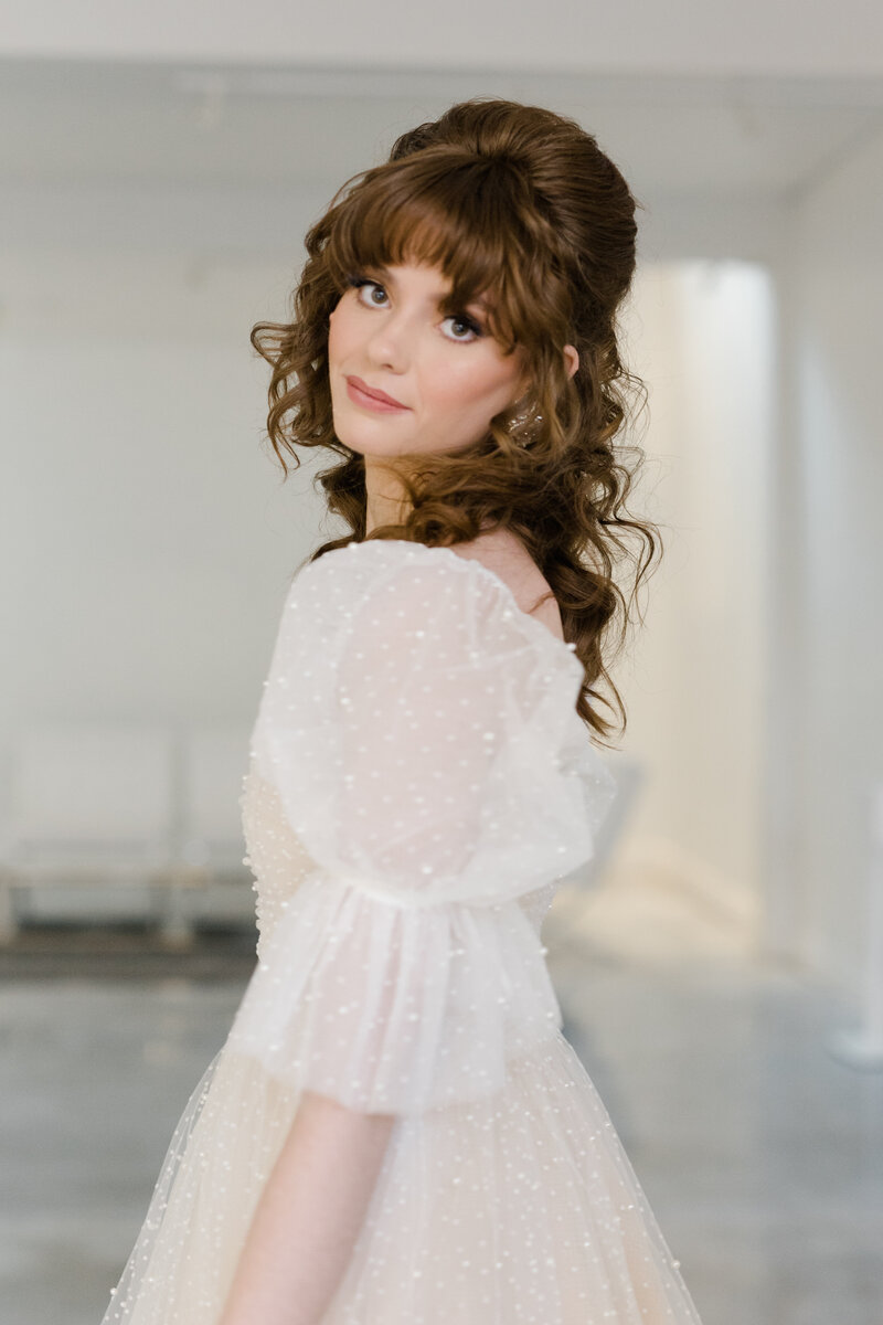Queer bride in sheer pearled white puff sleeve mini dress looking at camera smizing at Fathom Gallery in Georgetown 