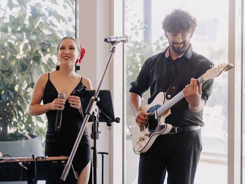 Stylish acoustic singer and guitarist duo performing at an indoor event with bridal‑style décor.
