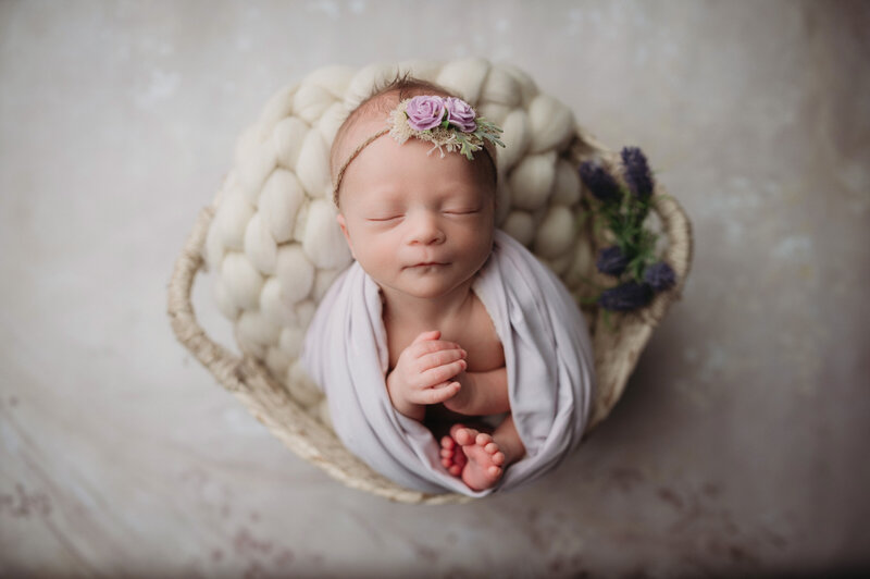 Beautiful newborn baby girl sleeping inside a basket while wrapped in soft lilac wrap with purple headband