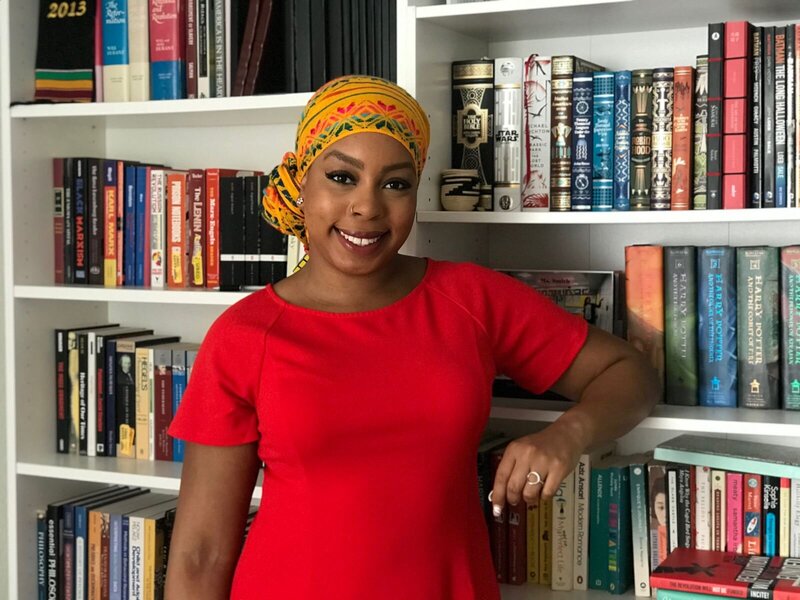 Deonna leaning by a bookcase