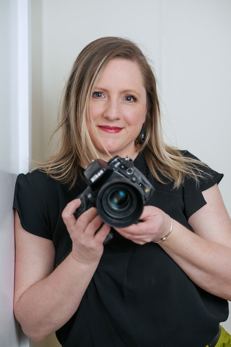 Creative headshot of Boston Branding Photographer Kristin Palkoner, owner of Lens and Prism Photographer holding her Nikon camera.
