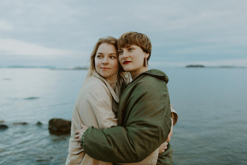Adult sisters standing and leaning their heads to each other by the sea in Kallahti in Helsinki