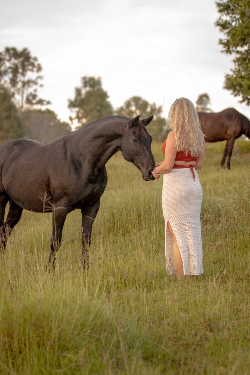 Woman in a white flowing skirt, embracing her femininity and gently connecting with horse during a horse retreat in Queensland, Australia. 