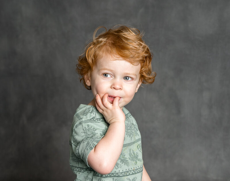 A young child in a green shirt poses with their head in their hands.