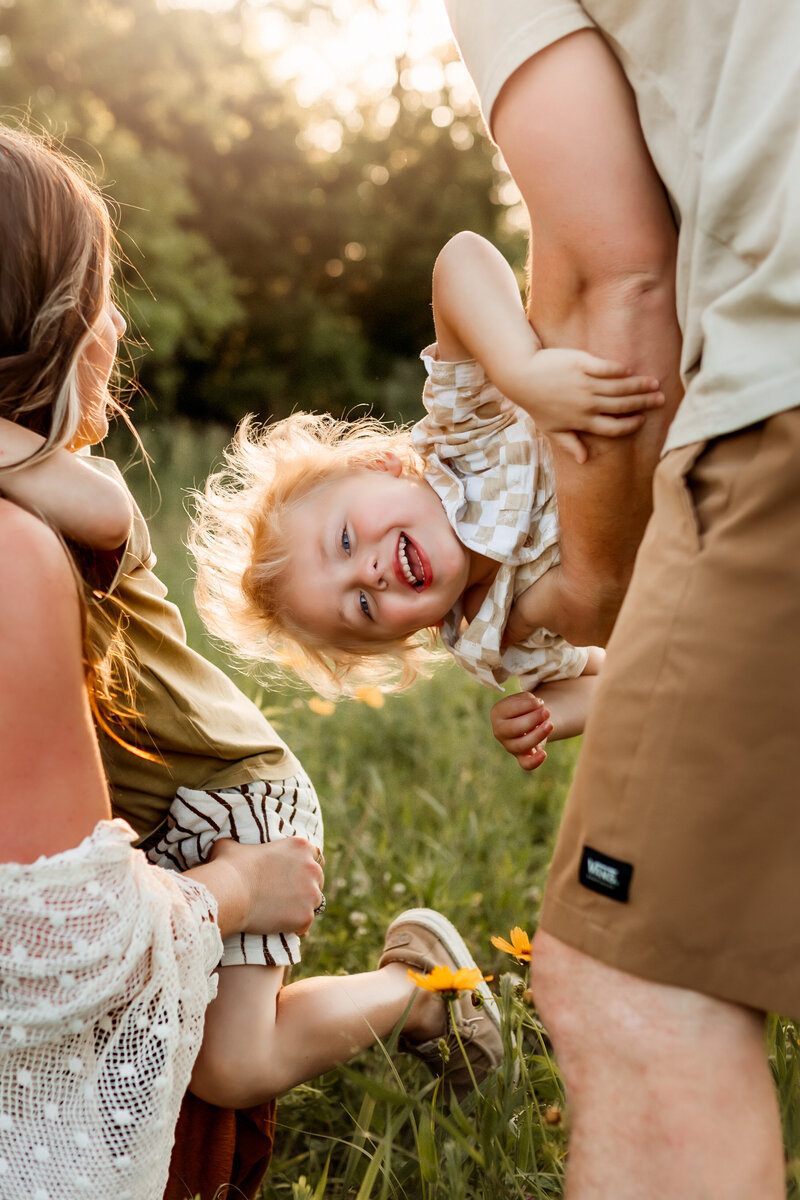 Little boy gets tipped sideways by his Dad in a field in Olathe during their family photoshoot